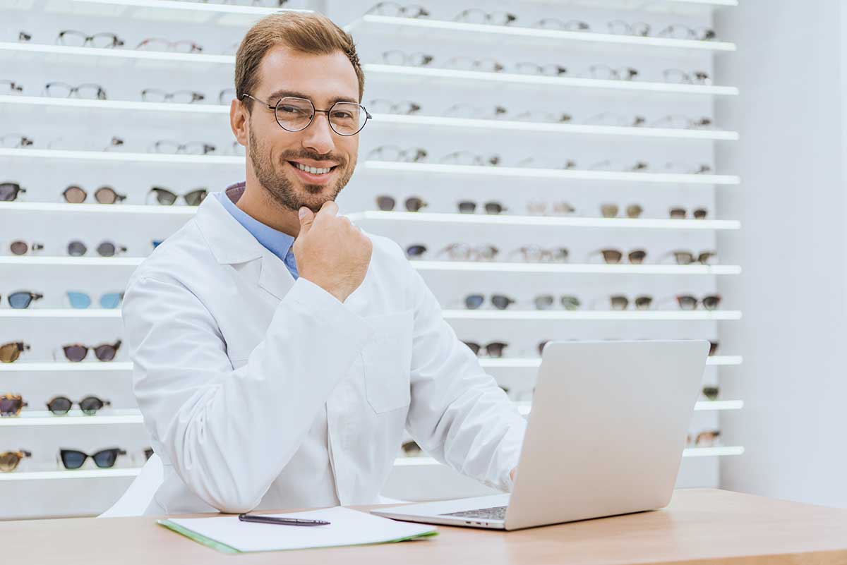 professional optician using laptop at table with papers in ophthalmic shop