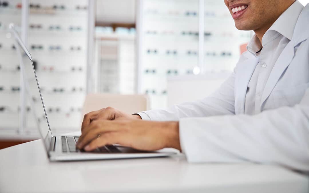 Merry young optometrist using laptop in the workplace