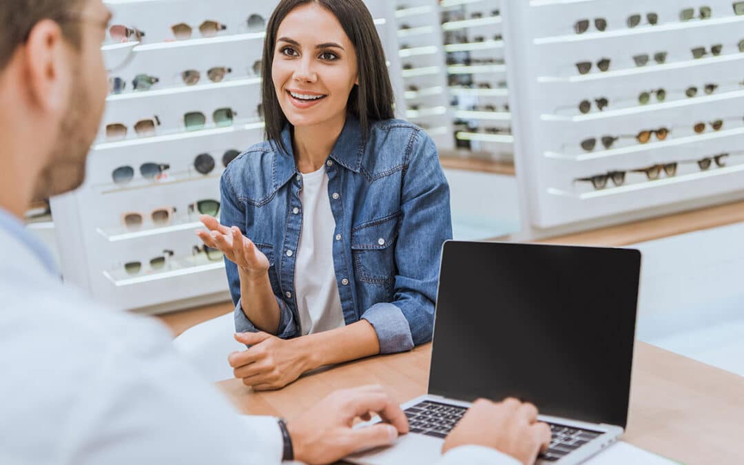 Customer talking with employee using laptop at eye clinic